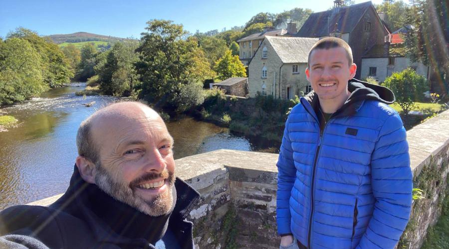Penpont Outdoorlads Event Leaders Craig and Tom stand on the bridge over the Usk with Penpont behind - where having met through ODL, they got married in Sept 2019